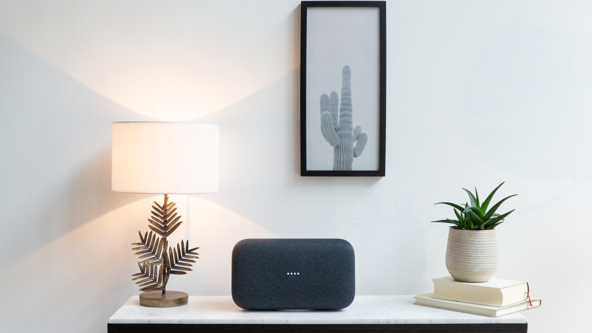 Google Home Max Der Google Home Max steht im Wohnzimmer zwischen Deko und einer Pflanze.