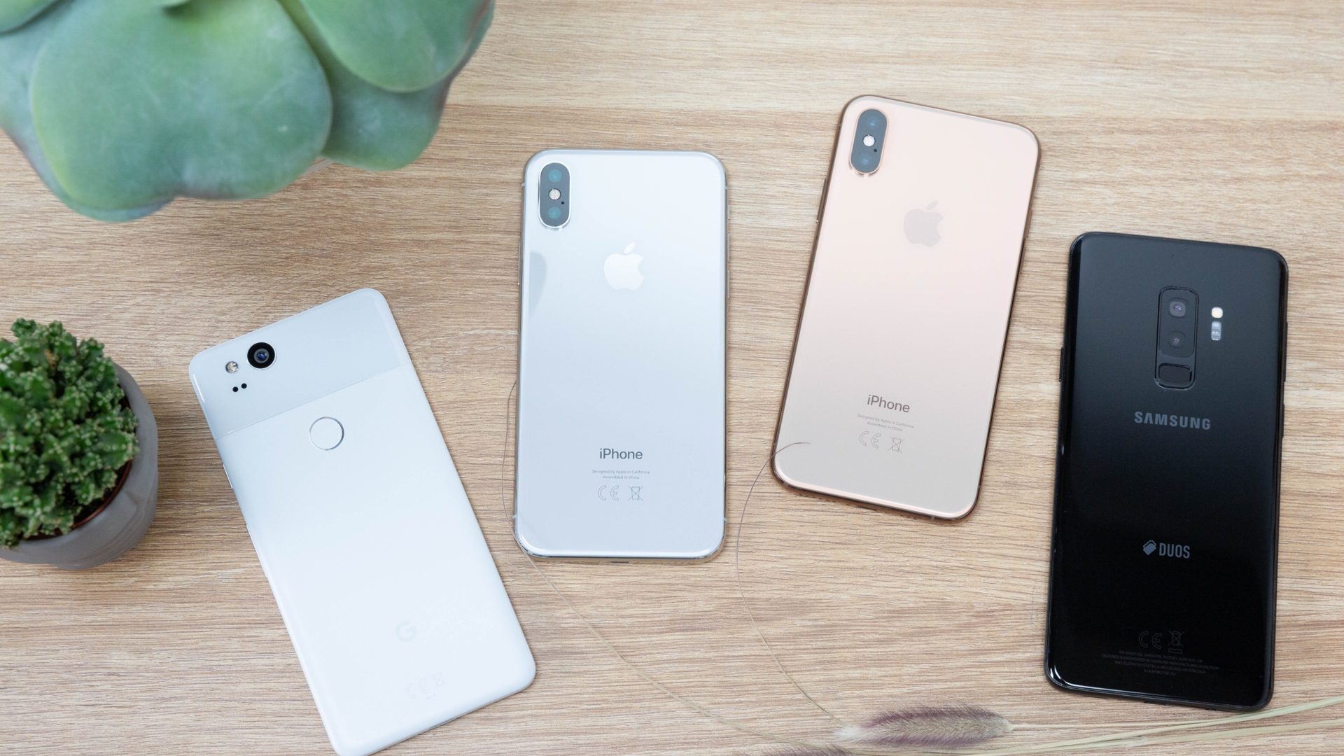 iPhone Xs, iPhone X, Galaxy S9 Plus und Pixel 2 im Kameravergleich Vier Smartphones liegen nebeneinander auf der Vorderseite. Man sieht ihre Rückseiten.