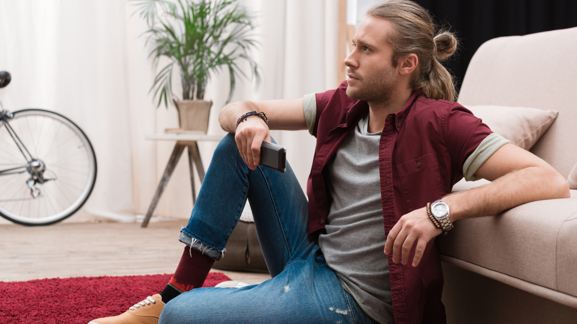 Mann, TV, Fernsehen. Wohnzimmer Mann sitzt auf dem Boden, mit Fernbedienung in der Hand.