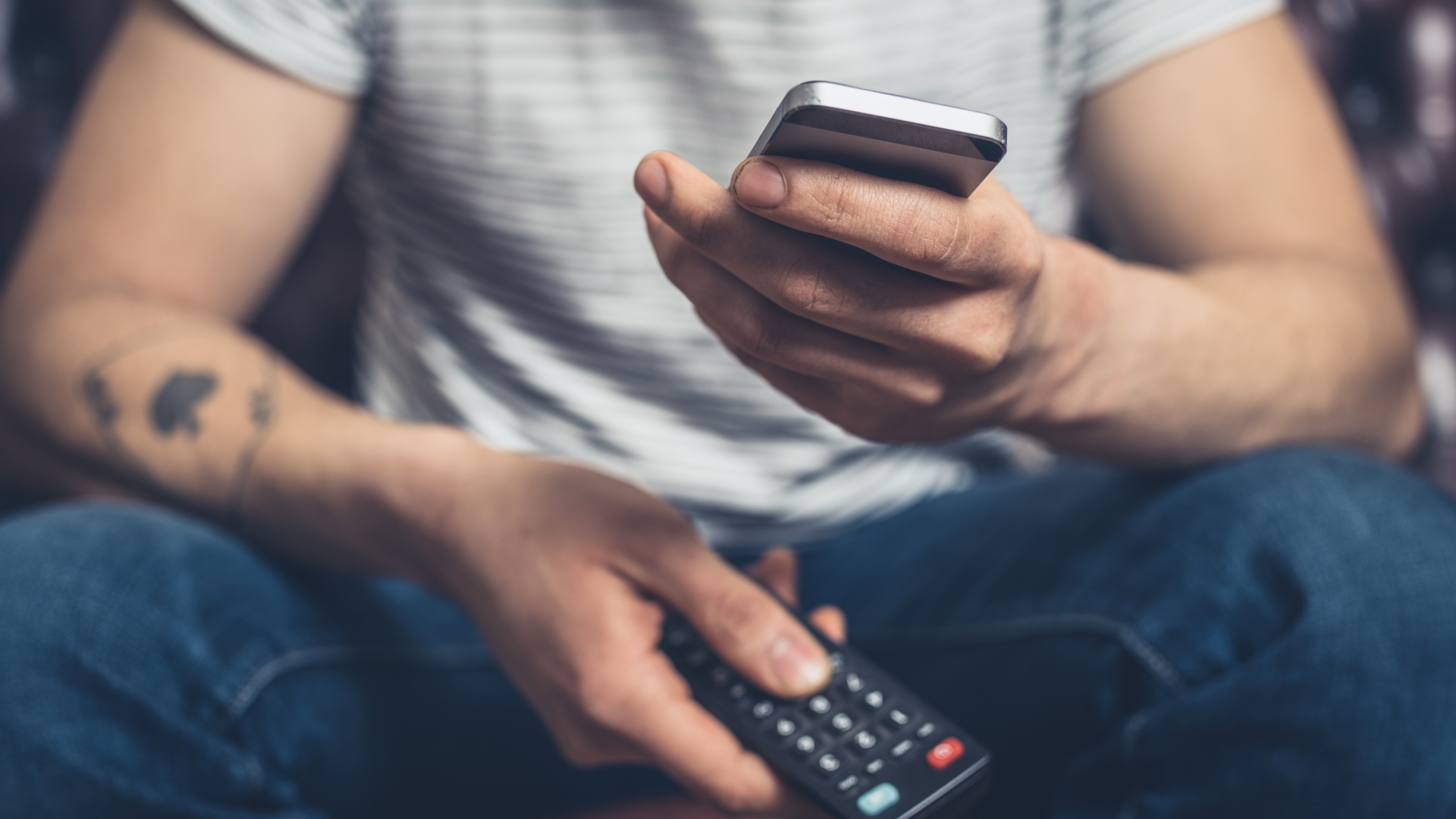 Mann, Smartphone, Fernsehen, Fernbedienung, Netflix Mann mit Fernbedienung und Handy in der Hand