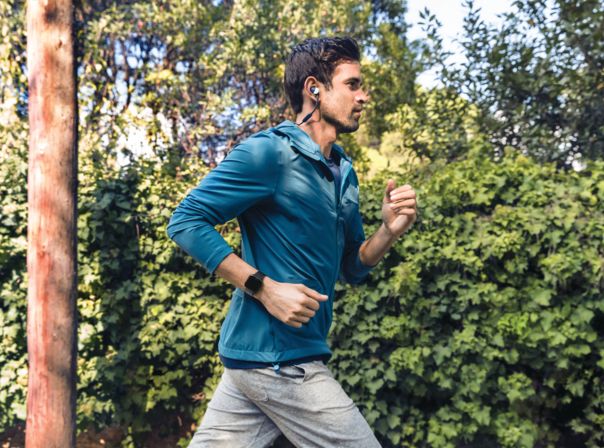 Fitbit Versa, Fitness-Tracker, Wearable Joggen, Sport, Kopfhörer Mann joggt im Wald