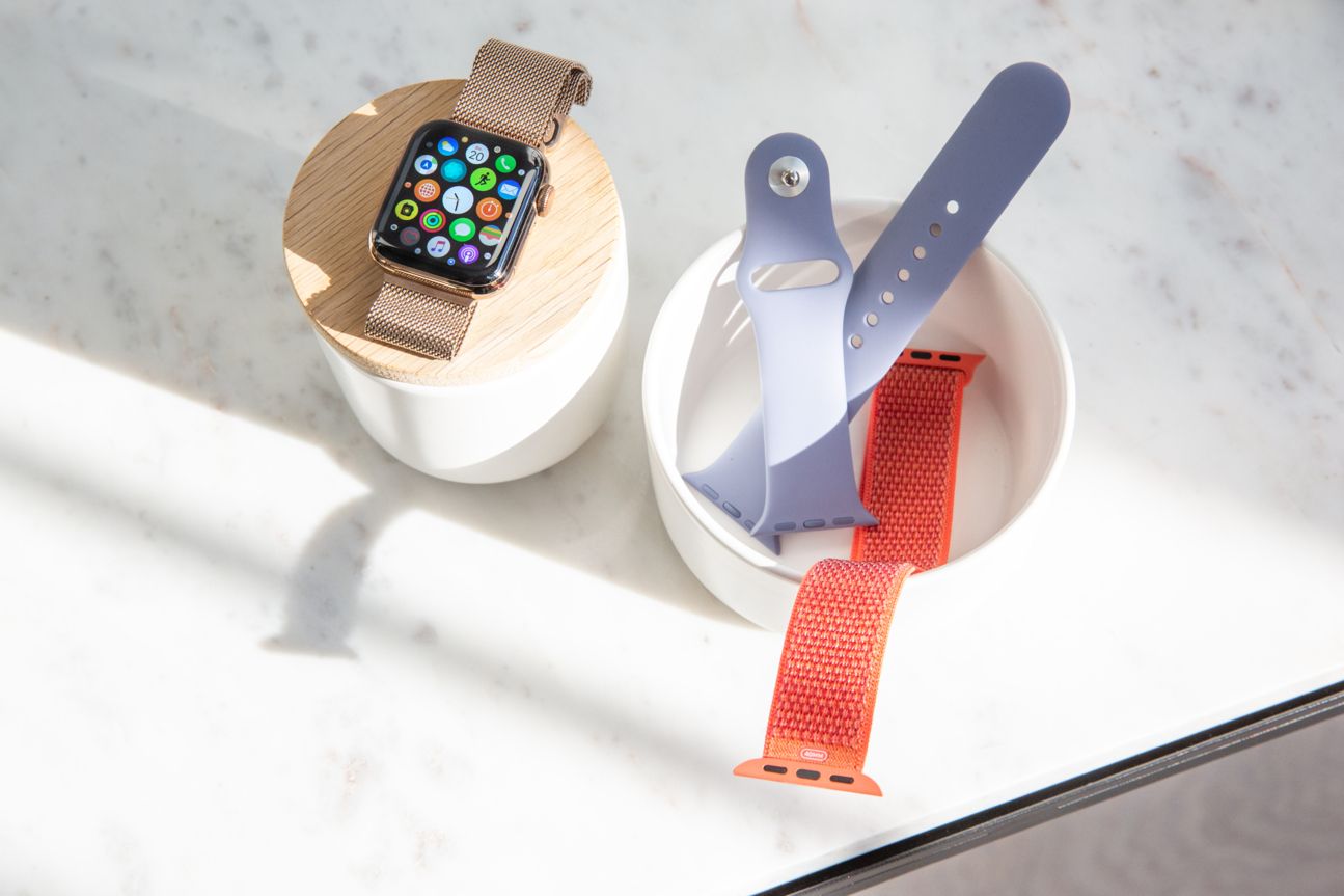 Die Apple Watch Series 4 auf einem Holzpodest neben einem Becher voller Armbänder.