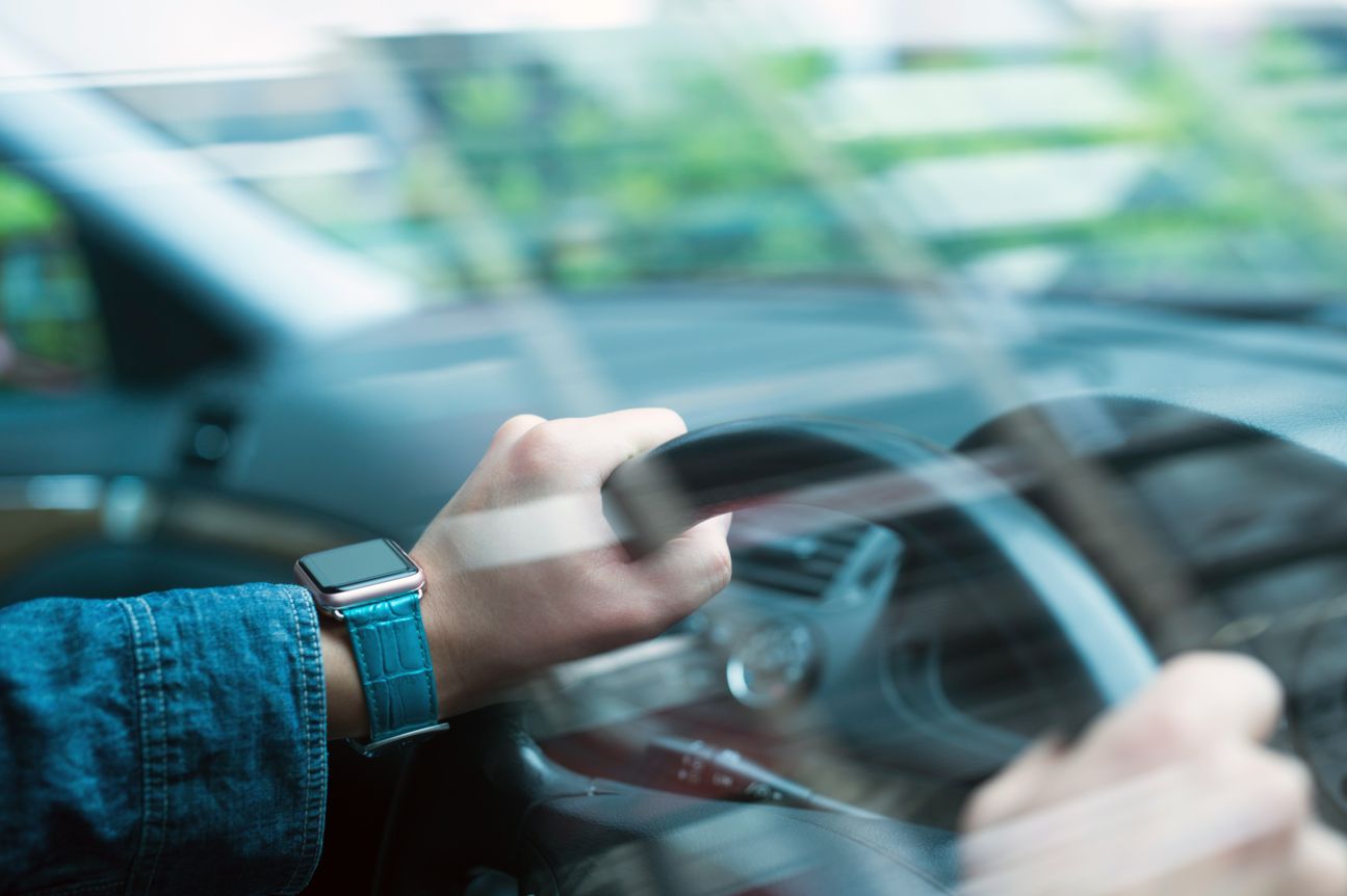 Autofahrer mit Smartwatch hat beide Hände am Lenkrad.